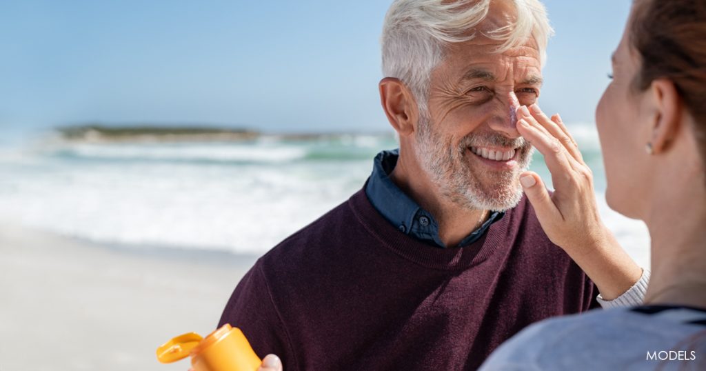 Woman applying sunscreen to a man's nose at the beach