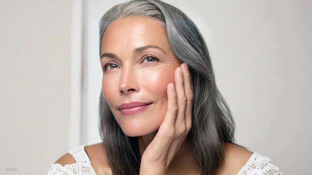 Mature woman smiling and resting her hand on her cheek. (Model)